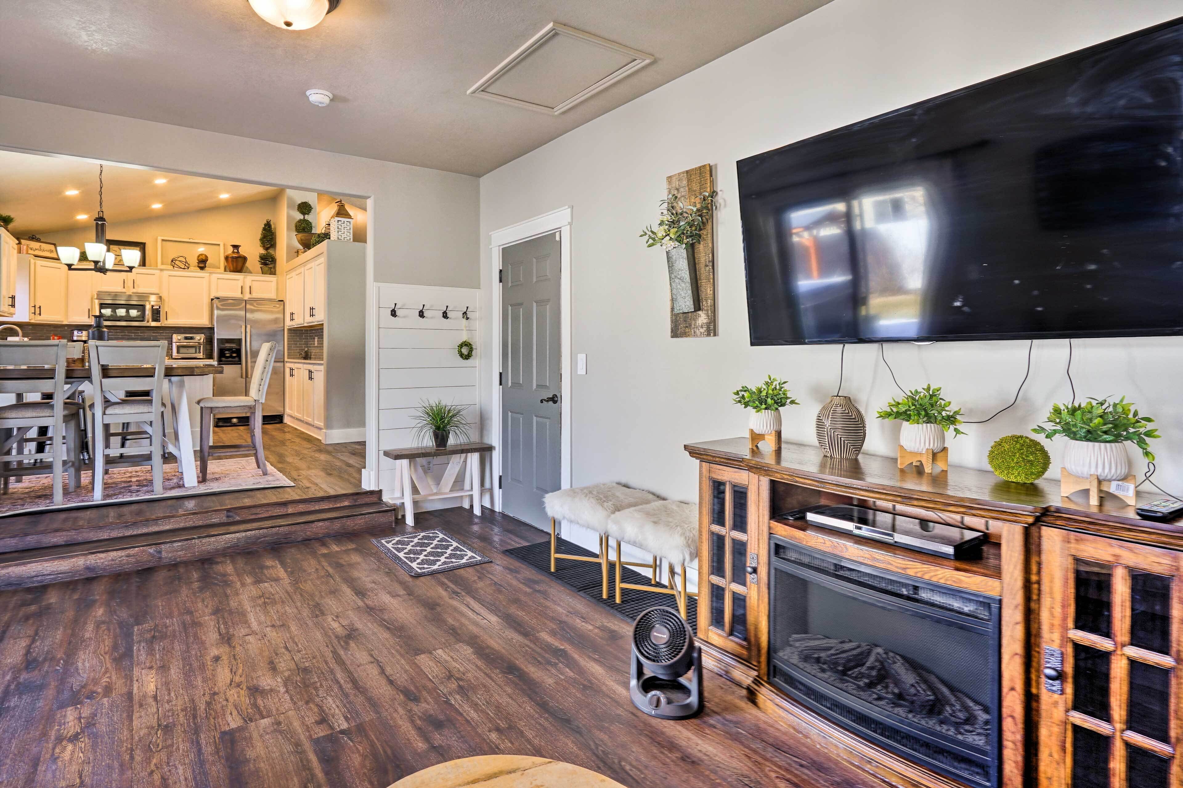 Una sala de estar moderna con chimenea, televisor montado en la pared y una cocina visible a través de una puerta abierta.