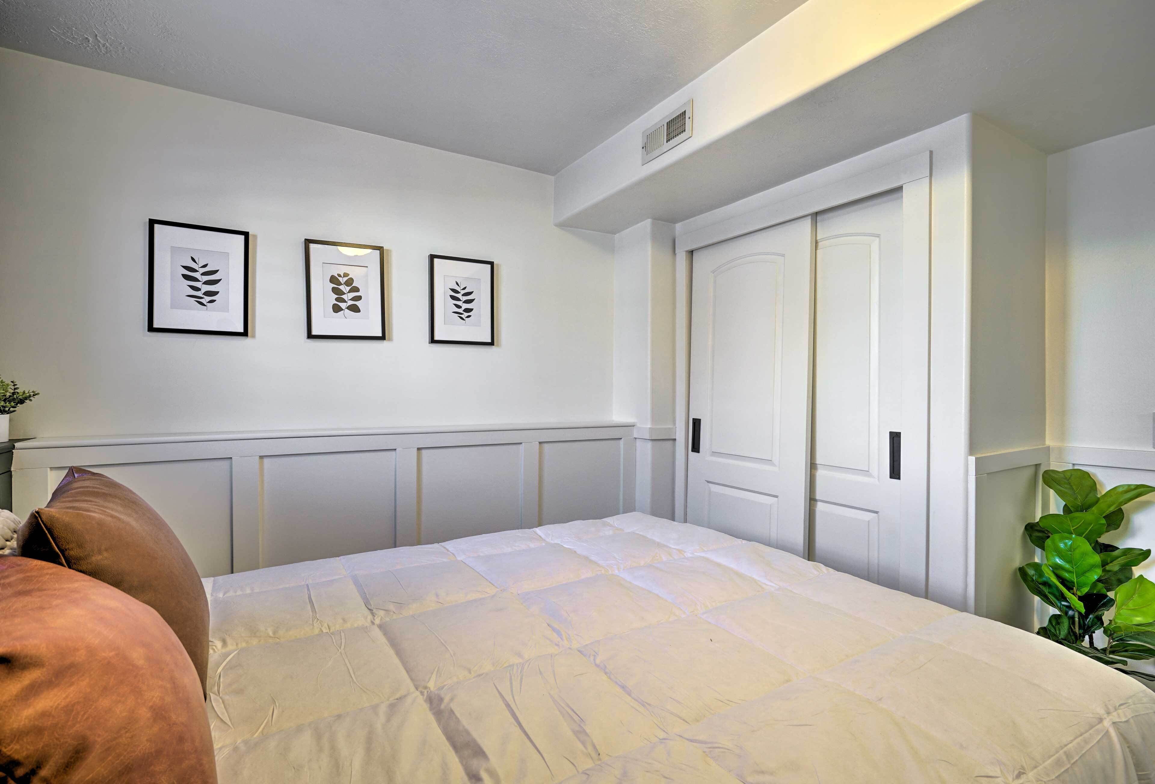 Une chambre à coucher avec un lit, des murs blancs, une porte et trois motifs de feuilles encadrées accrochés au mur.
