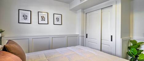Une chambre à coucher avec un lit, des murs blancs, une porte et trois motifs de feuilles encadrées accrochés au mur.