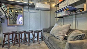 A room with a grey couch, wooden stools, a mirror, and shelves with various items.