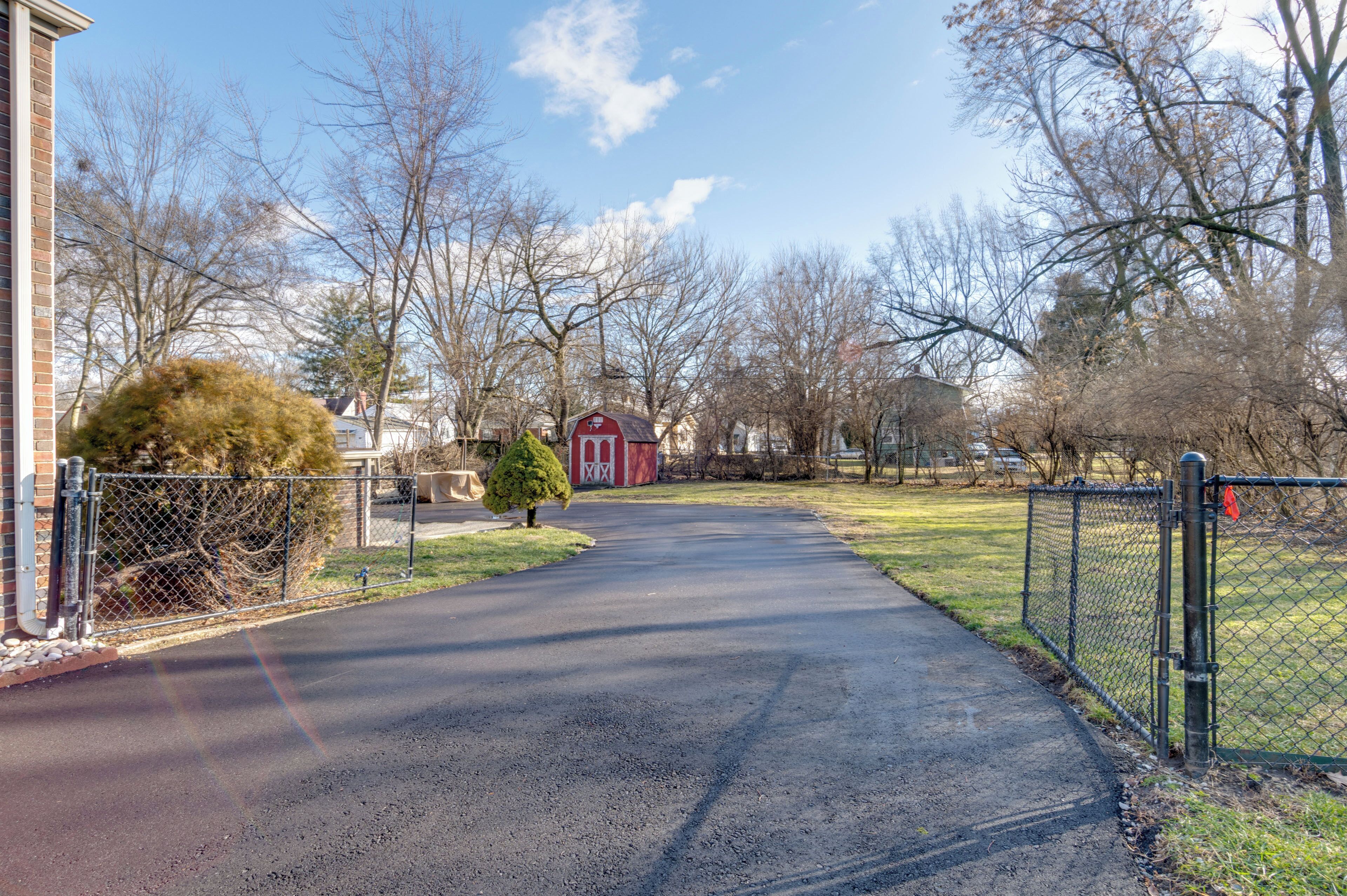 A paved driveway leading to a red barn in a rural setting with bare trees and a clear sky.