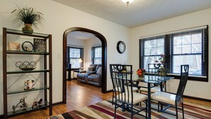 A dining area with a glass table and chairs, a striped rug, and a bookshelf with decorative items. - Idyllic Home Near Indianapolis Motor Speedway (Indianapolis)