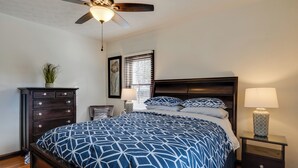 A bedroom with a large bed, a ceiling fan, a dresser, a nightstand, and a window with blinds. - Idyllic Home Near Indianapolis Motor Speedway (Indianapolis)
