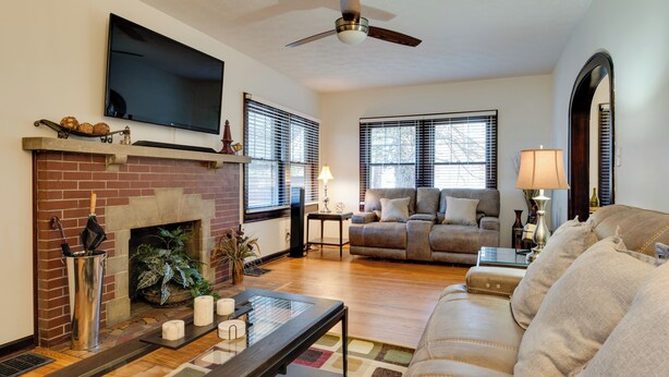 A living room with a fireplace, a flat-screen TV, a ceiling fan, a sofa, and a coffee table. - Idyllic Home Near Indianapolis Motor Speedway (Indianapolis)