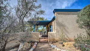 A building with a covered patio area, a stone pathway leading to the entrance, and a view of the surrounding landscape.
