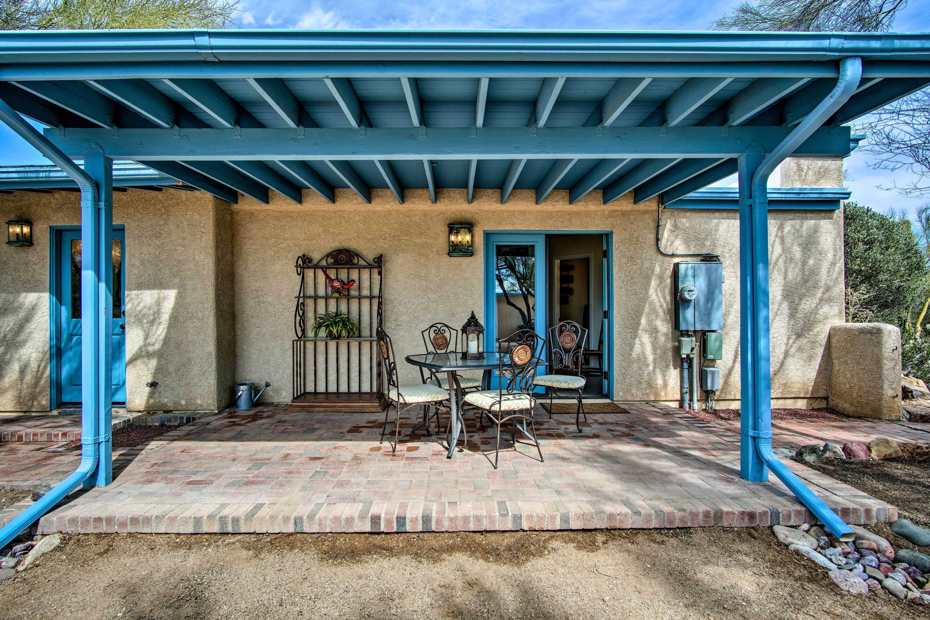 Une terrasse couverte avec un sol en briques, du mobilier d’extérieur et une pergola aux poutres bleues.