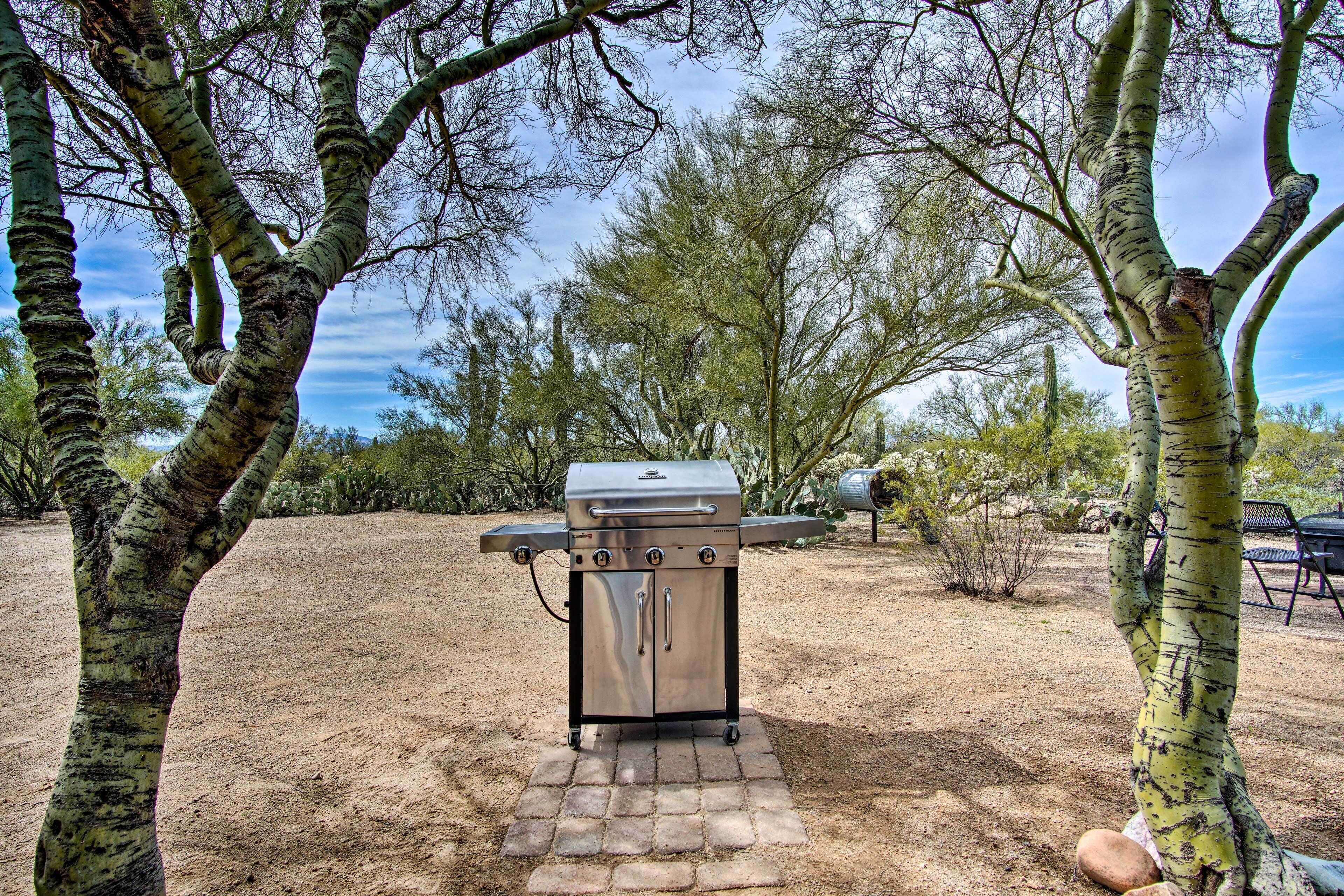 A portable grill set up in a desert-like environment with sparse vegetation and a clear sky.