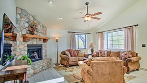 A spacious living room with a stone fireplace, two sofas, a coffee table, and a ceiling fan.