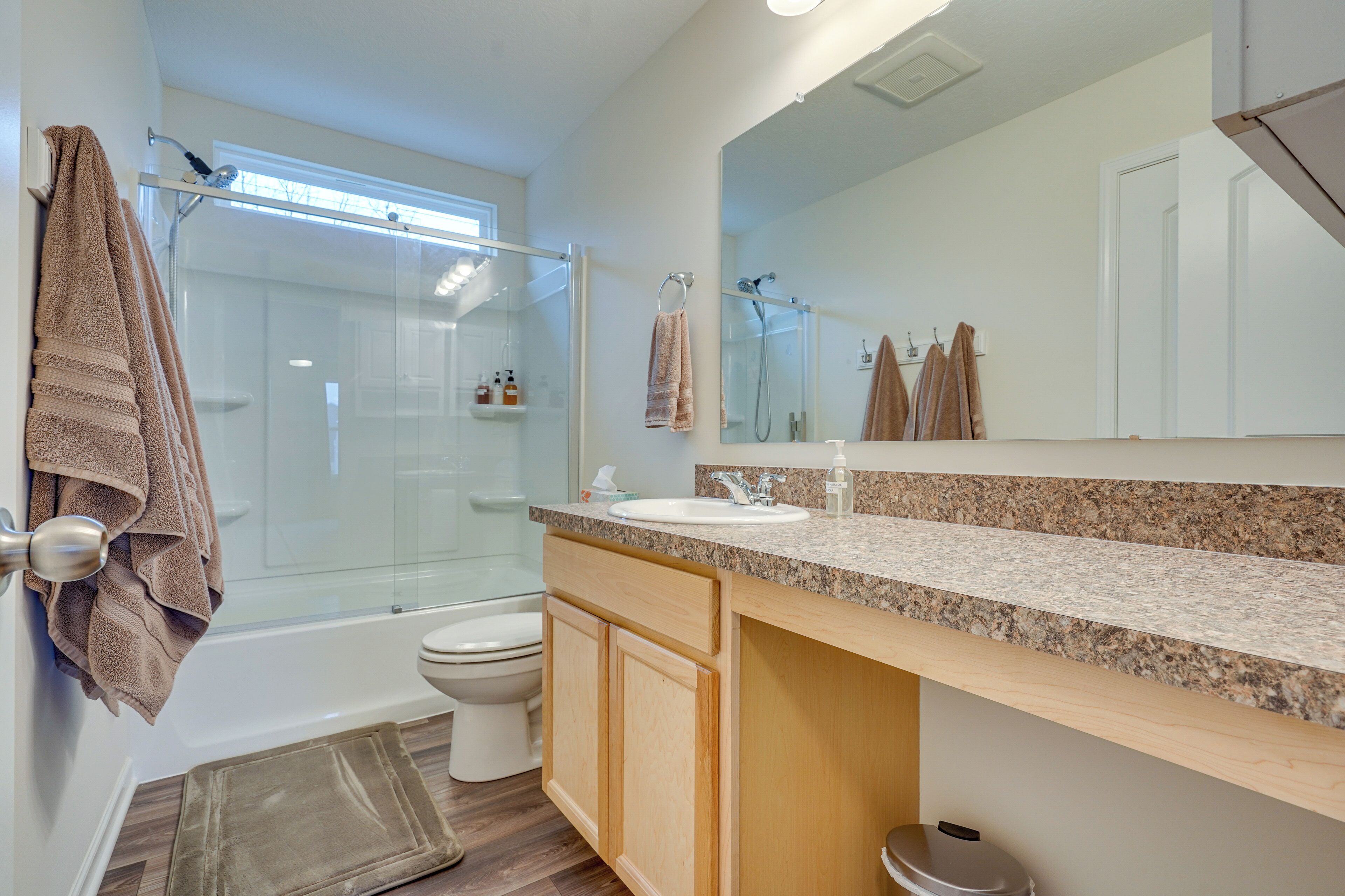 A modern bathroom with a glass-enclosed shower, a white toilet, and a granite countertop sink.