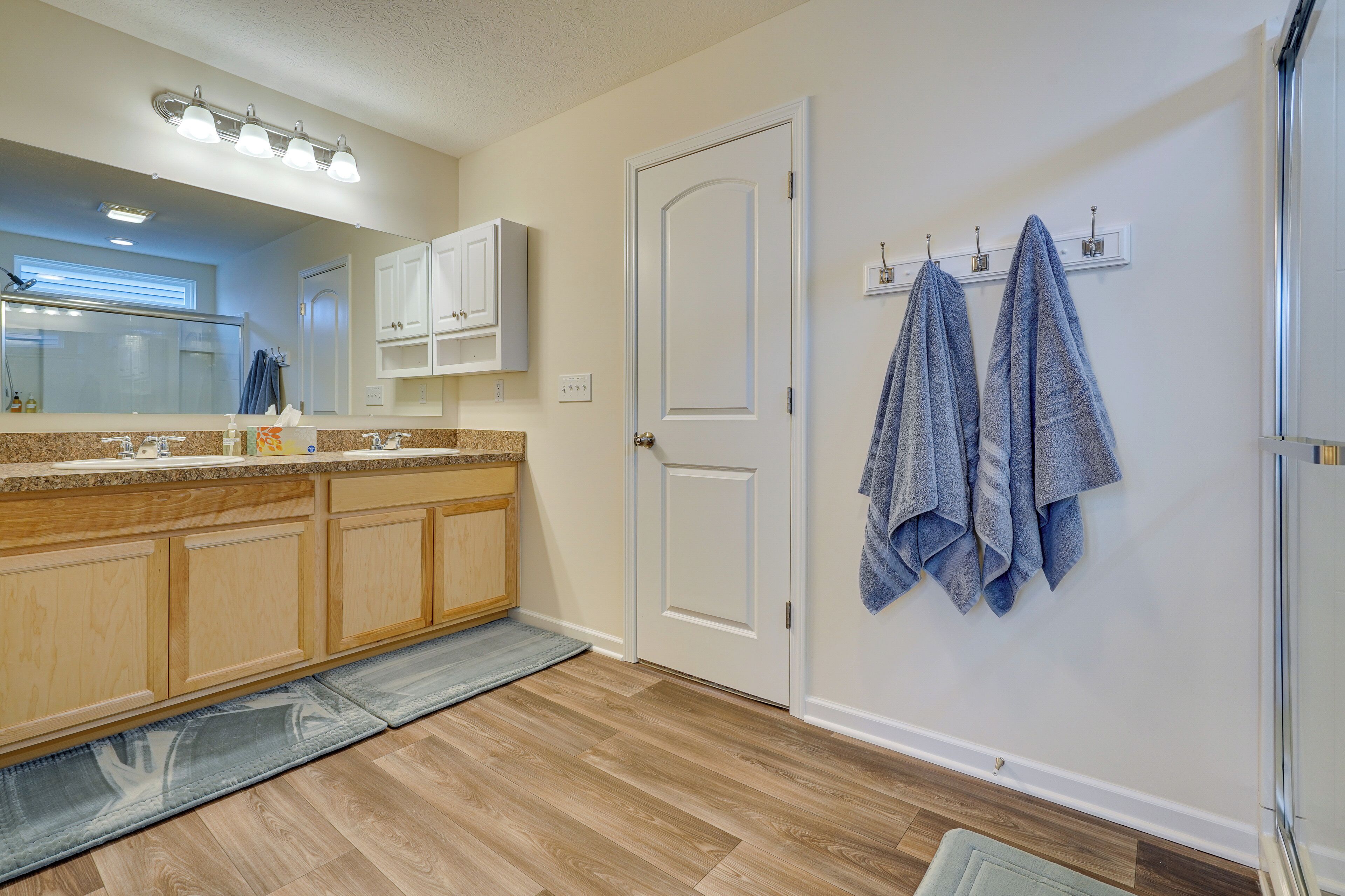 A modern bathroom with a wooden vanity, a large mirror, and a towel rack with two towels.