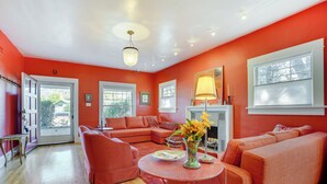 A living room with a sectional sofa, a round coffee table, and a fireplace. There are two windows and a door leading outside.