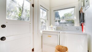 A laundry room with a white door, two windows, a washing machine, a dryer, and a wicker basket.