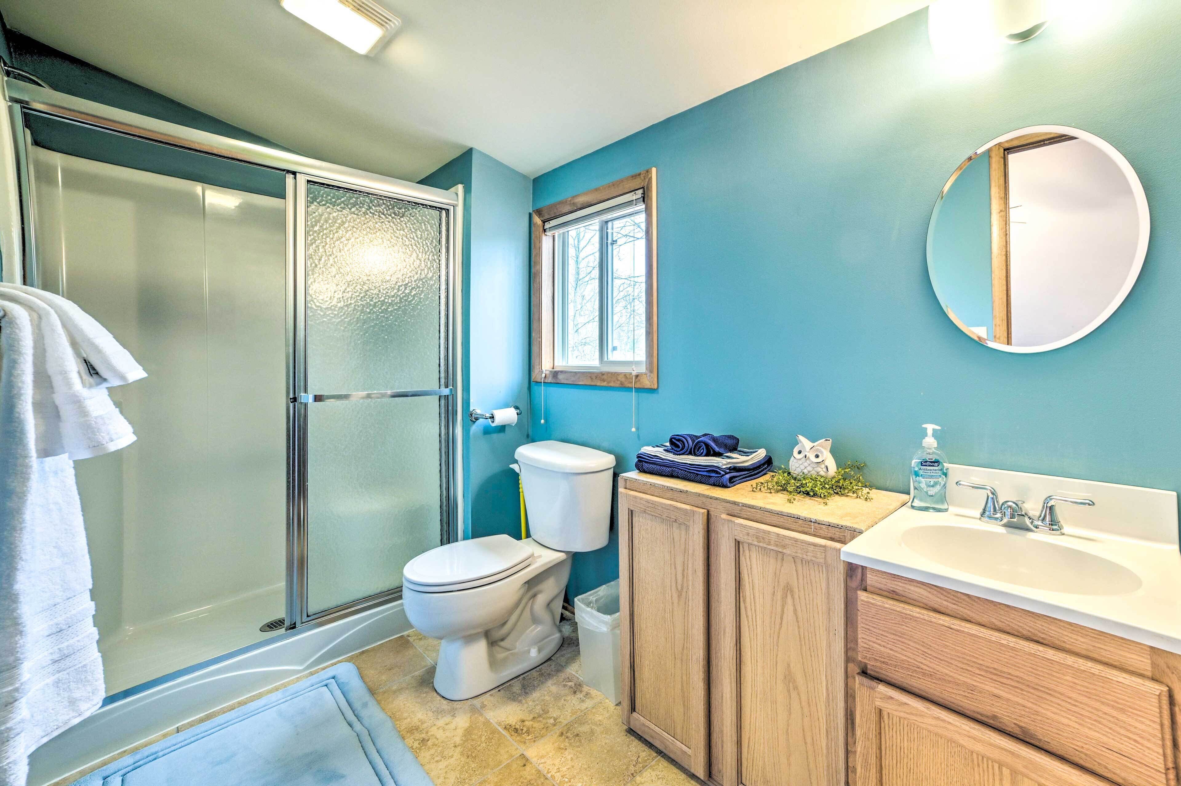 A bathroom with a glass shower enclosure, a toilet, a sink with a mirror, and wooden cabinets.