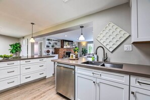 A modern kitchen with white cabinetry, a stainless steel dishwasher, and a brick backsplash. - 7 Mi to Downtown Phoenix: Home w/ Pool & Foosball! (Phoenix)