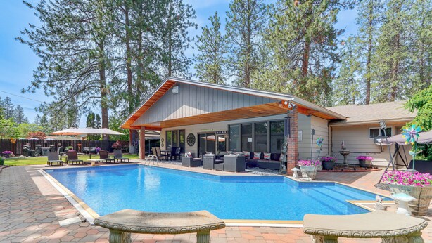 Una piscina con un patio techado, zona de estar al aire libre y un banco de piedra.