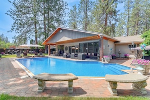 A swimming pool with a covered patio area, outdoor seating, and a stone bench. - Spokane Valley Vacation Rental w/ Shared Pool! (Spokane Valley)
