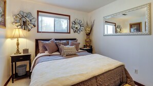Un dormitorio ordenado con cama, mesitas de noche, lámpara, espejos decorativos y una ventana.