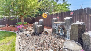 Un jardín con cerca de madera, un árbol y rocas decorativas.