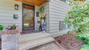 Una casa con porche delantero, buzón, arreglo floral y una pequeña maceta de ladrillo.