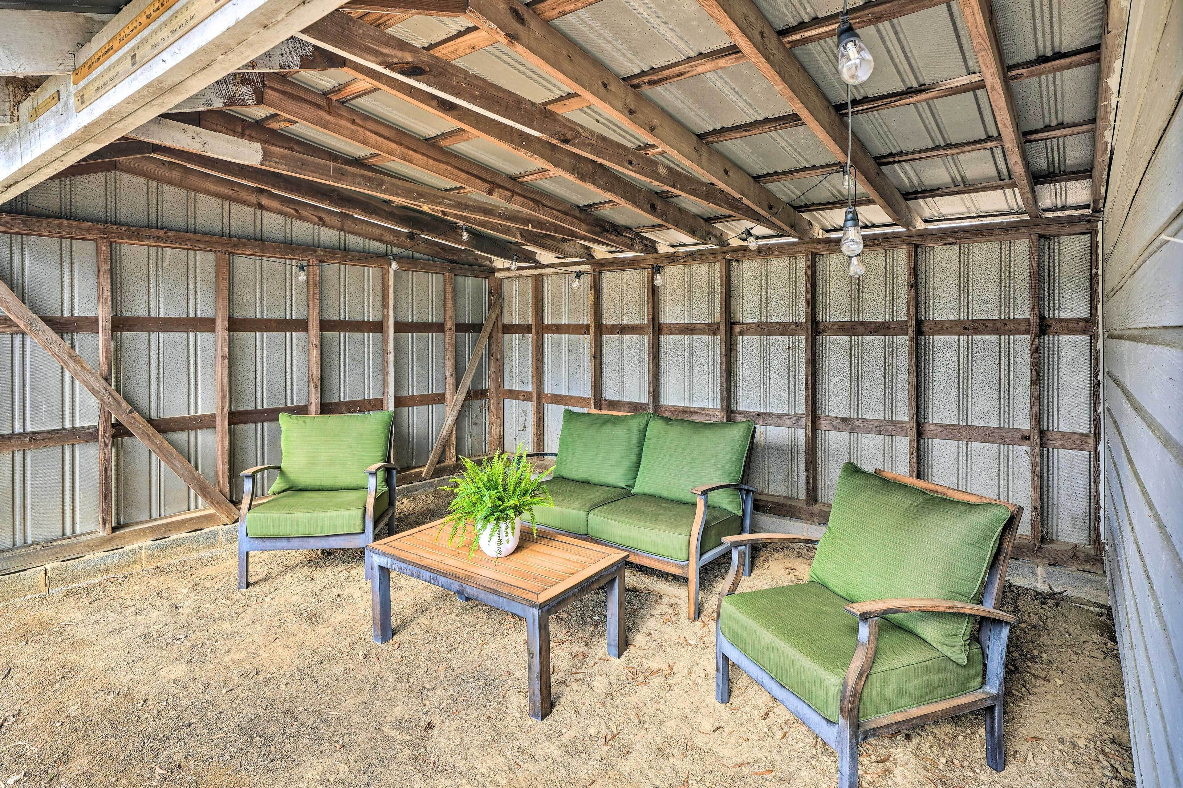 A rustic barn interior with wooden beams, a green cushioned sofa, and a wooden coffee table with a plant.