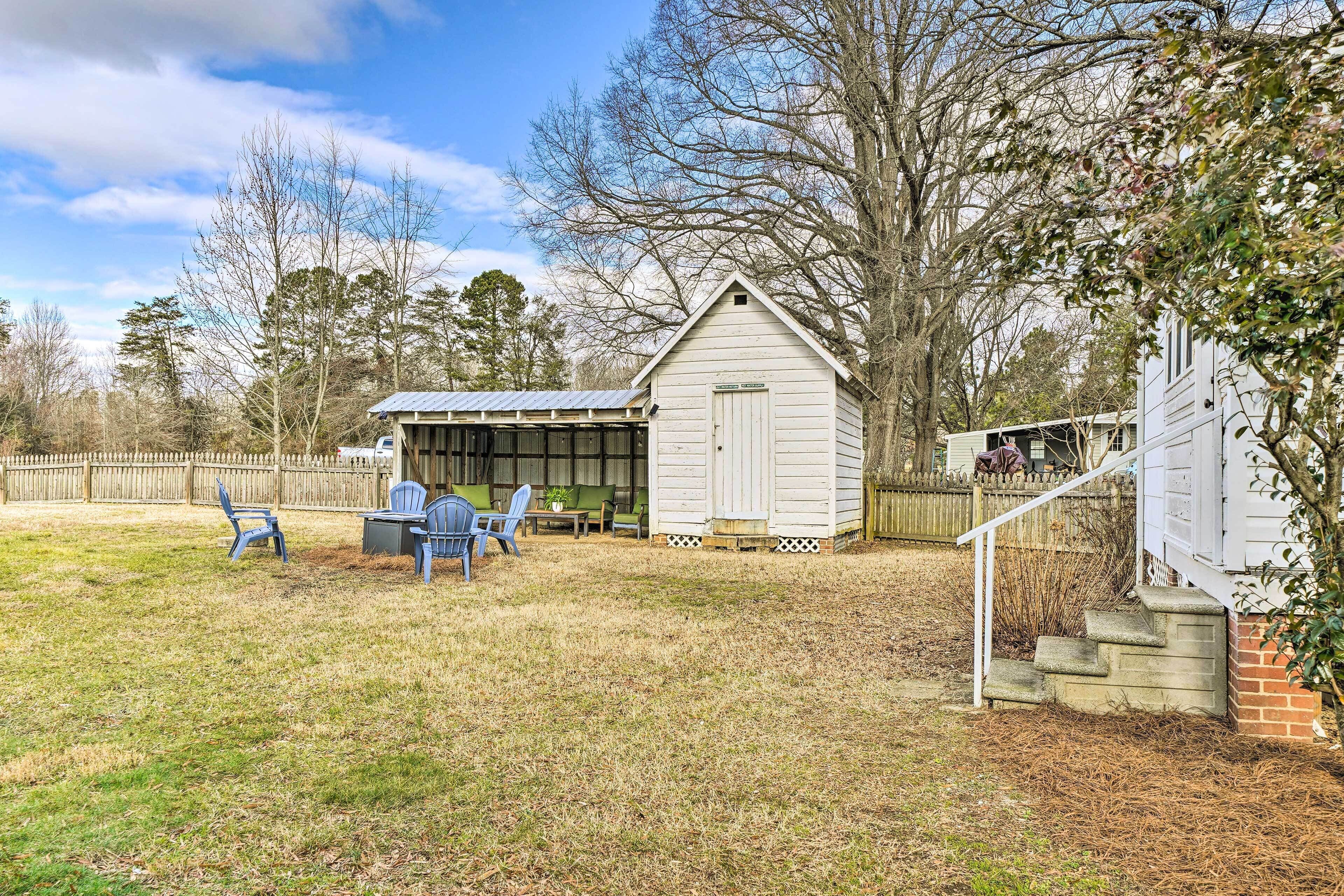 A wooden shed with a covered porch, a brick staircase, and a fenced backyard with a lawn and chairs.