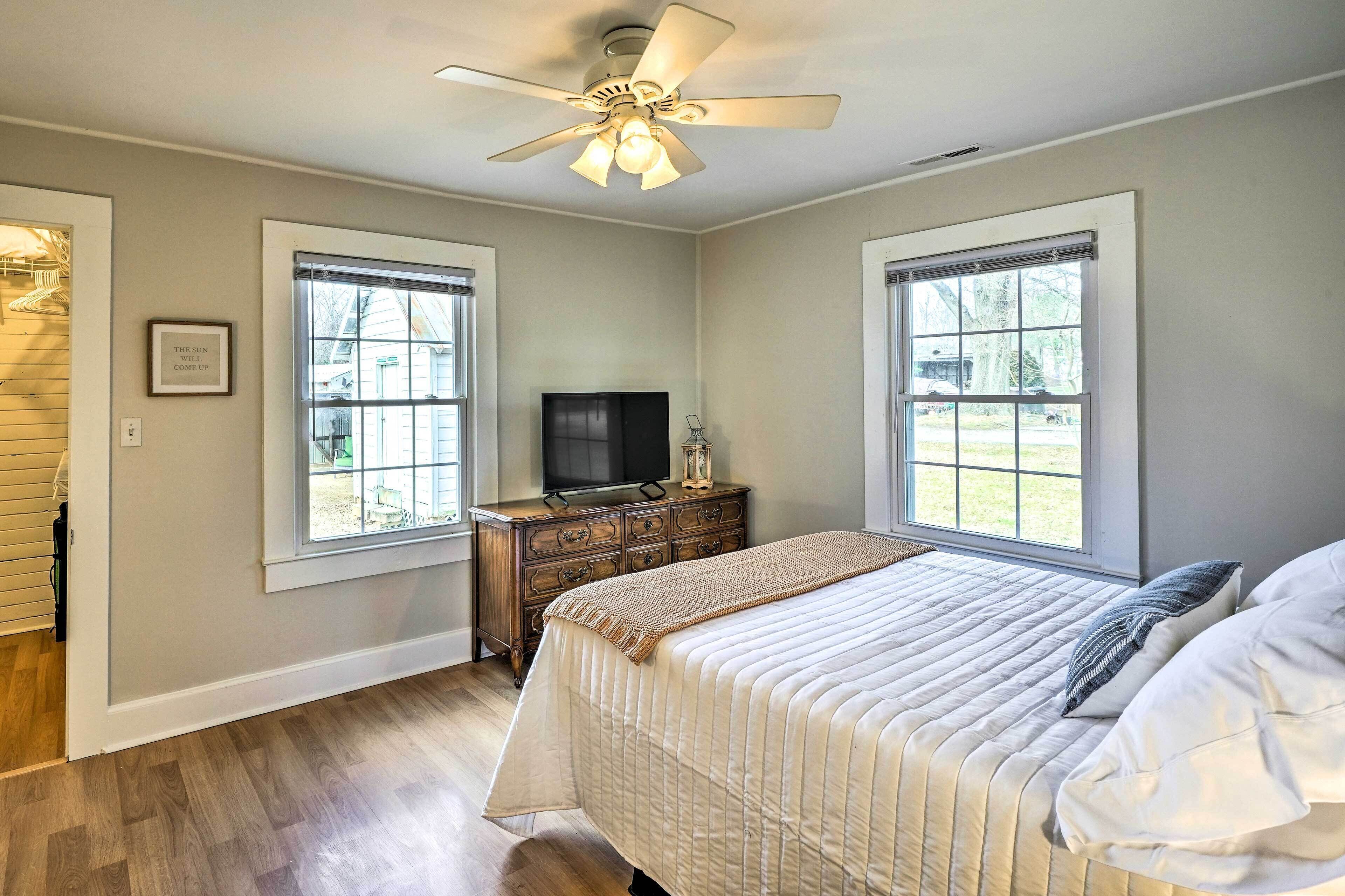 A bedroom with a bed, a dresser, a television, and two windows.