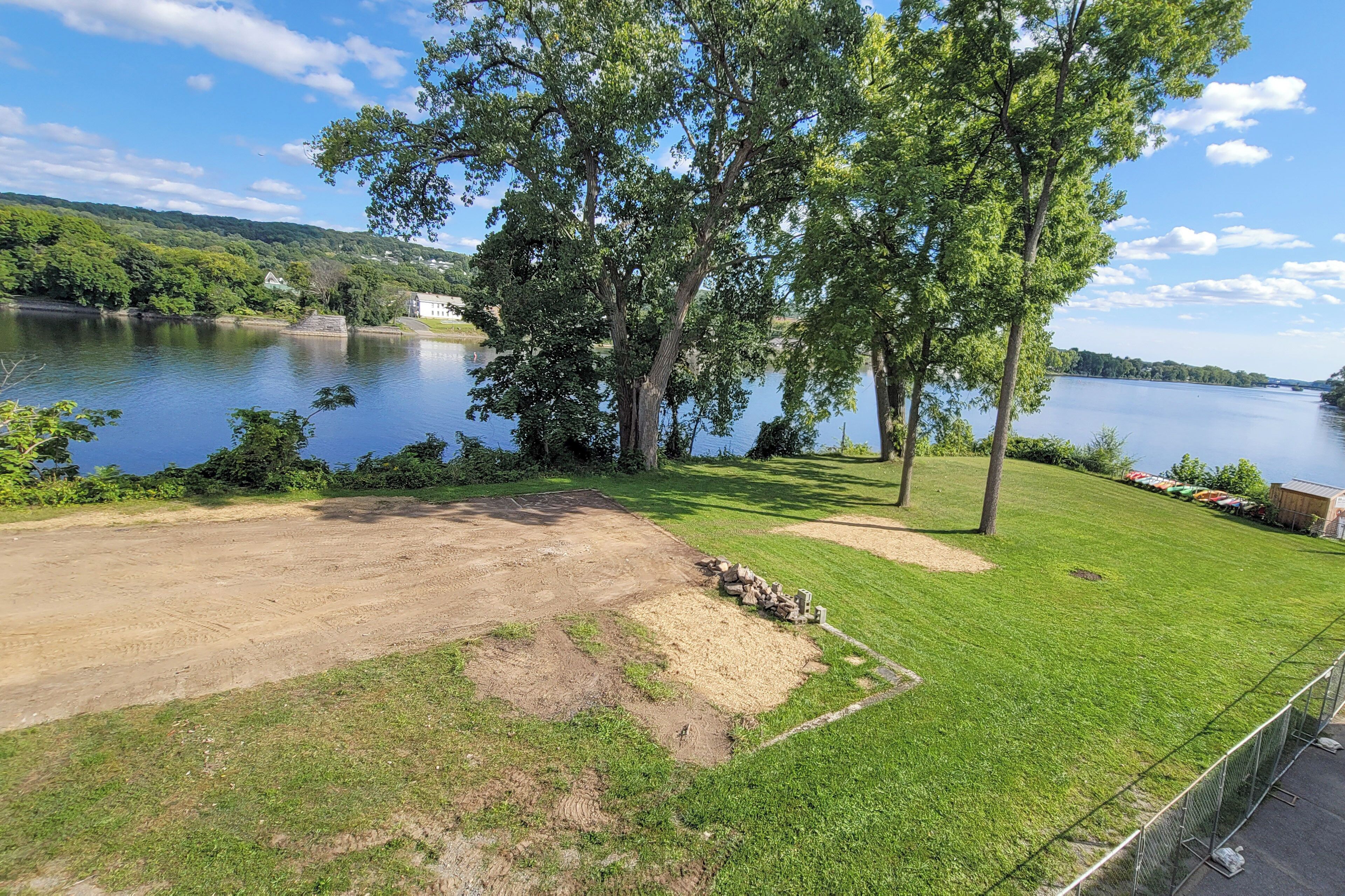 A grassy area with a dirt path leading to a body of water, surrounded by trees and a fence.