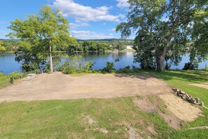 Un camping con zona de tierra, árboles y un lago al fondo.