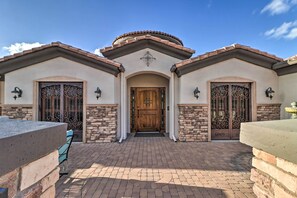 Stucco and stone building with a central entrance, flanked by decorative gates, and a paved patio area.