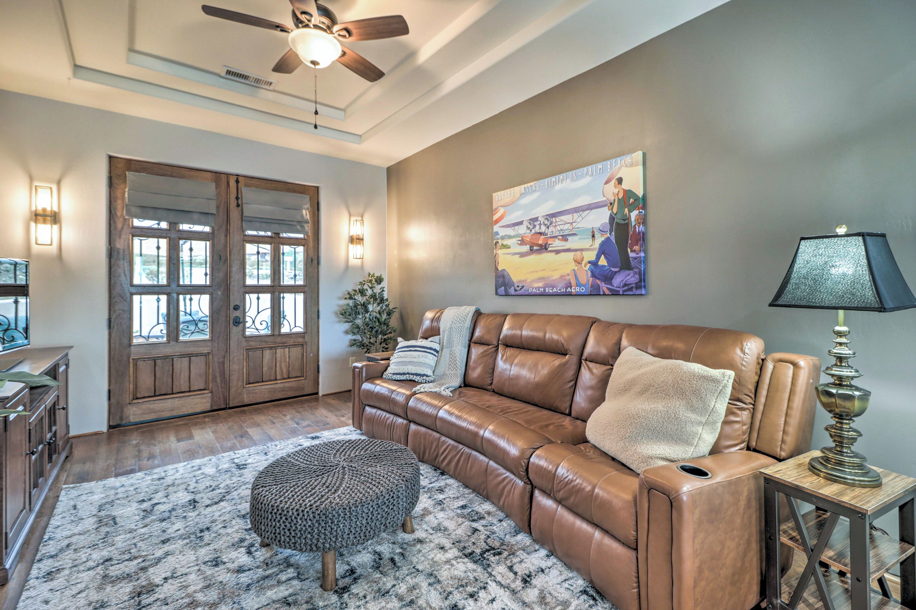 A living room with a brown leather sofa, a round ottoman, a wooden side table with a lamp, and a painting on the wall.