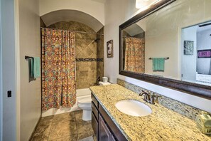 Un baño con lavamanos de encimera de granito, un espejo grande y una ducha con cortina estampada.