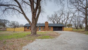 A house with a gravel driveway, a wooden fence, and a large tree in front. - Chandler Vacation Rental on Route 66, Near Casino (Chandler)