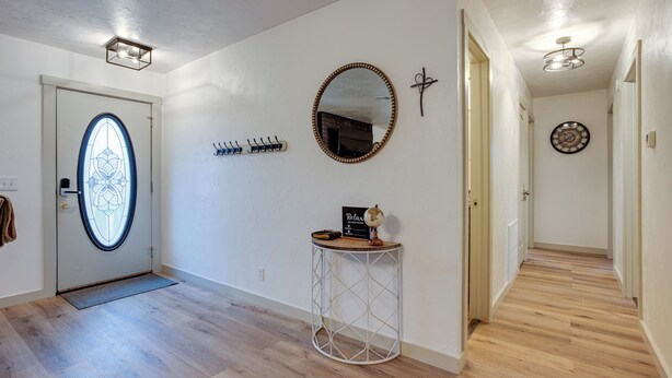 A hallway with a wooden floor, a round mirror with a wooden frame, a small side table with a globe and a clock, and a door with a stained glass window. - Chandler Vacation Rental on Route 66, Near Casino (Chandler)