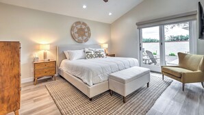 A bedroom with a large bed, a ceiling fan, a nightstand with a lamp, a chair, and a view of the outdoors through a sliding door. - Luxury Scottsdale Vacation Rental w/ Patio! (Scottsdale)