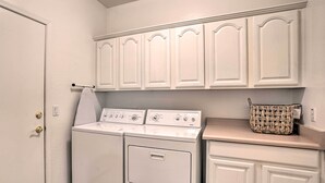 Une buanderie équipée d’un lave-linge et d’un sèche-linge à chargement frontal, avec des meubles blancs au-dessus et un panier en osier posé sur le plan de travail.