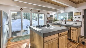 A modern kitchen with wooden cabinets, a large island, and a view of a snowy landscape through glass doors. - 8 Mi to Heavenly Mtn Resort! Hot Tub Hideaway (South Lake Tahoe)