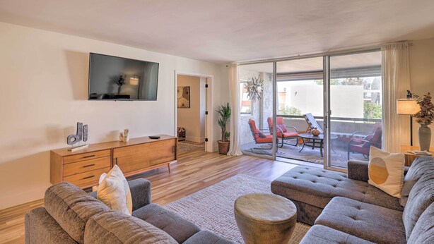 A modern living room with a sofa set, a wooden cabinet, a flat-screen TV, and a sliding glass door leading to an outdoor seating area.