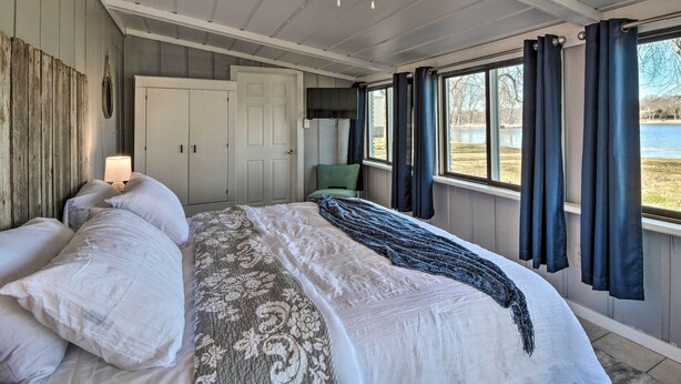 A bedroom with a bed, a ceiling fan, a TV, and a view of a lake. - Riverfront Dixon, Illinois, Vacation Rental! (Dixon)