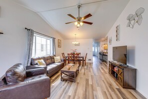 A living room with a sofa, coffee table, dining table, ceiling fan, and a TV on a stand. - Family-friendly Columbia Falls Townhome w/ Views! (Columbia Falls)