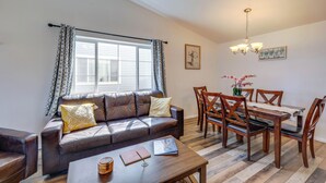 Una sala de estar con un sofá de cuero marrón, una mesa de comedor de madera y sillas, una mesita de centro con un libro y una vela, y un candelabro.