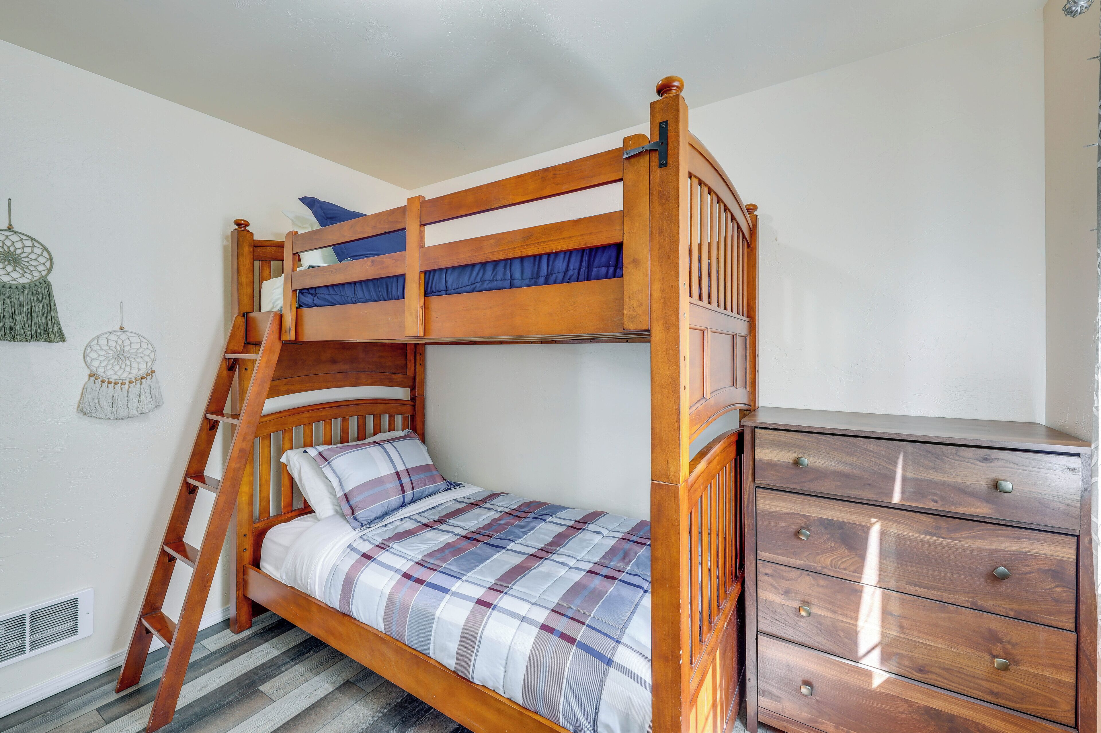 A bunk bed with a ladder, a wooden dresser, and a wall-mounted decorative item.