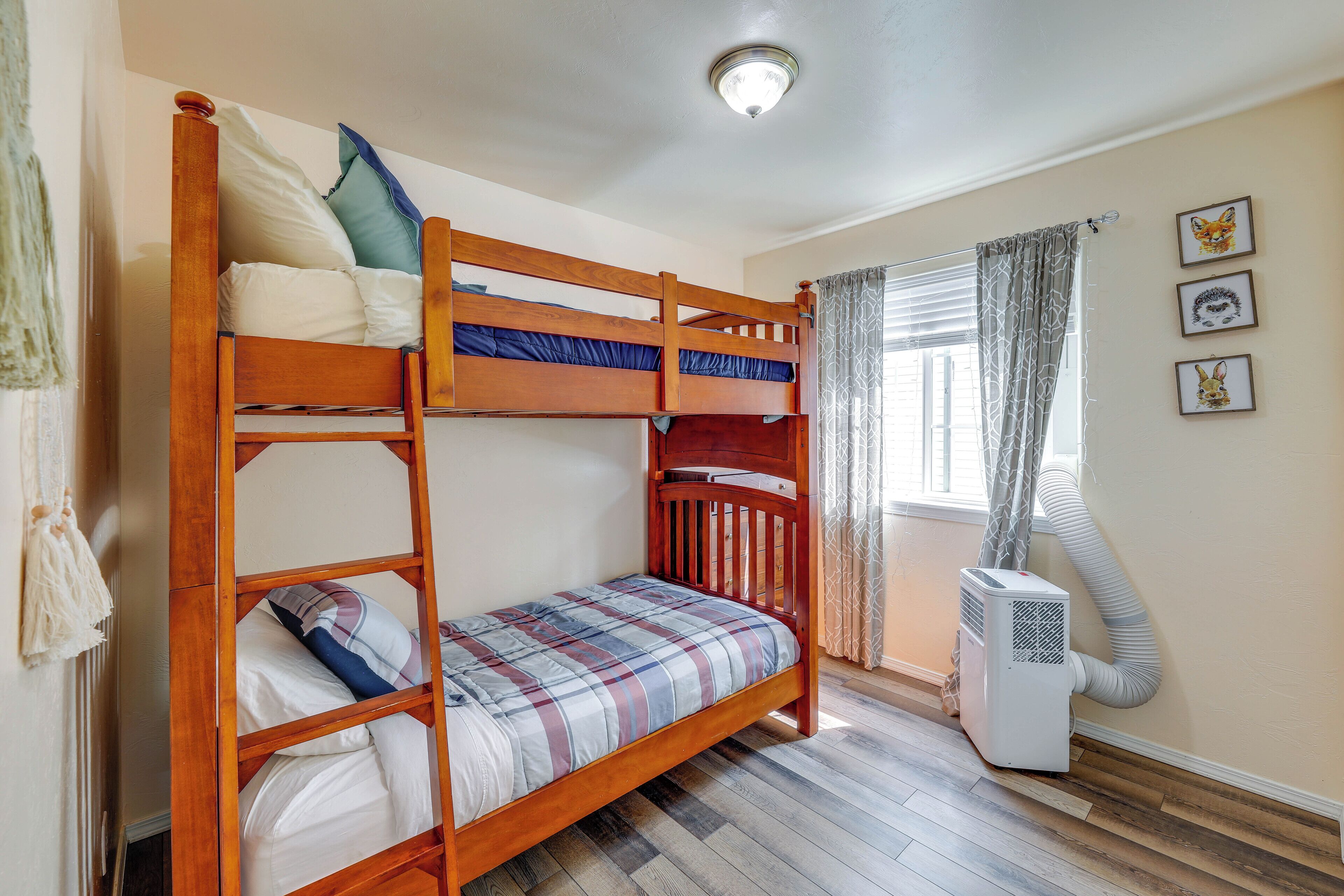 A bunk bed room with a window, curtains, and a wall-mounted air conditioner.