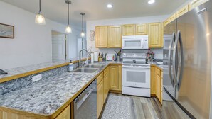 Cocina con encimeras de granito, armarios de madera y electrodomésticos de acero inoxidable, con iluminación colgante.