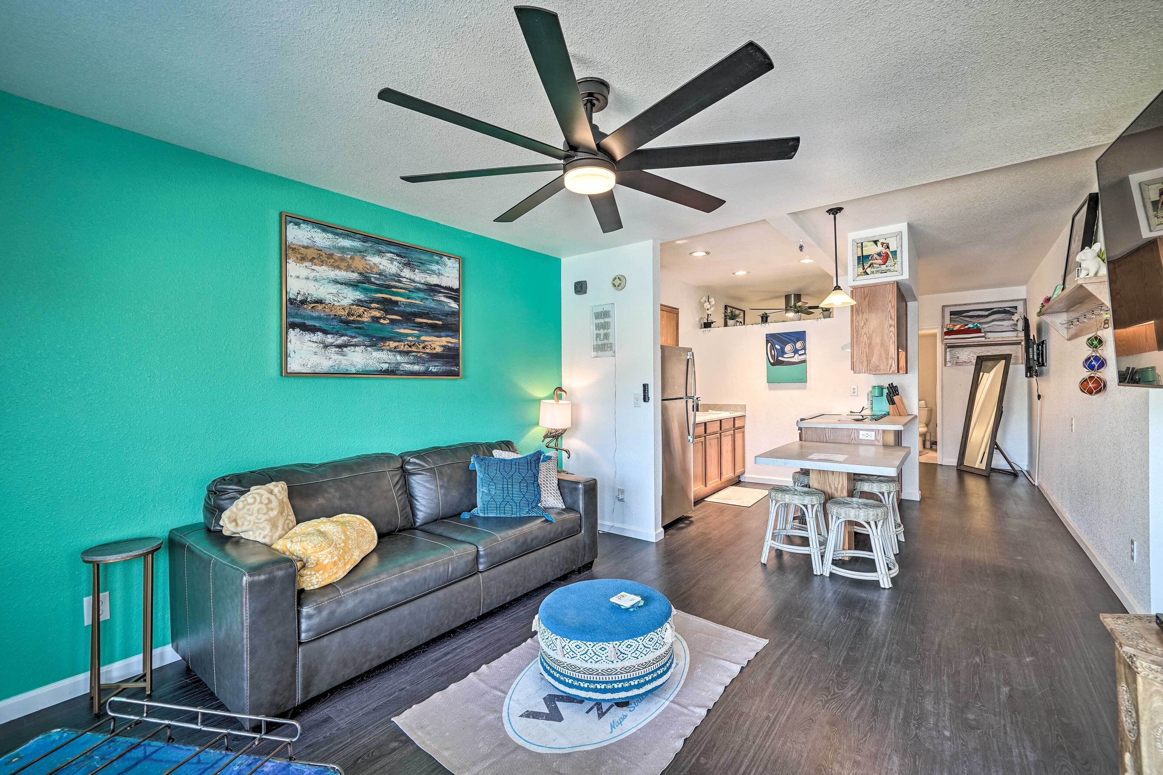 Un salon avec un canapé en cuir marron foncé, un pouf rond, un ventilateur de plafond et un mur de couleur turquoise.