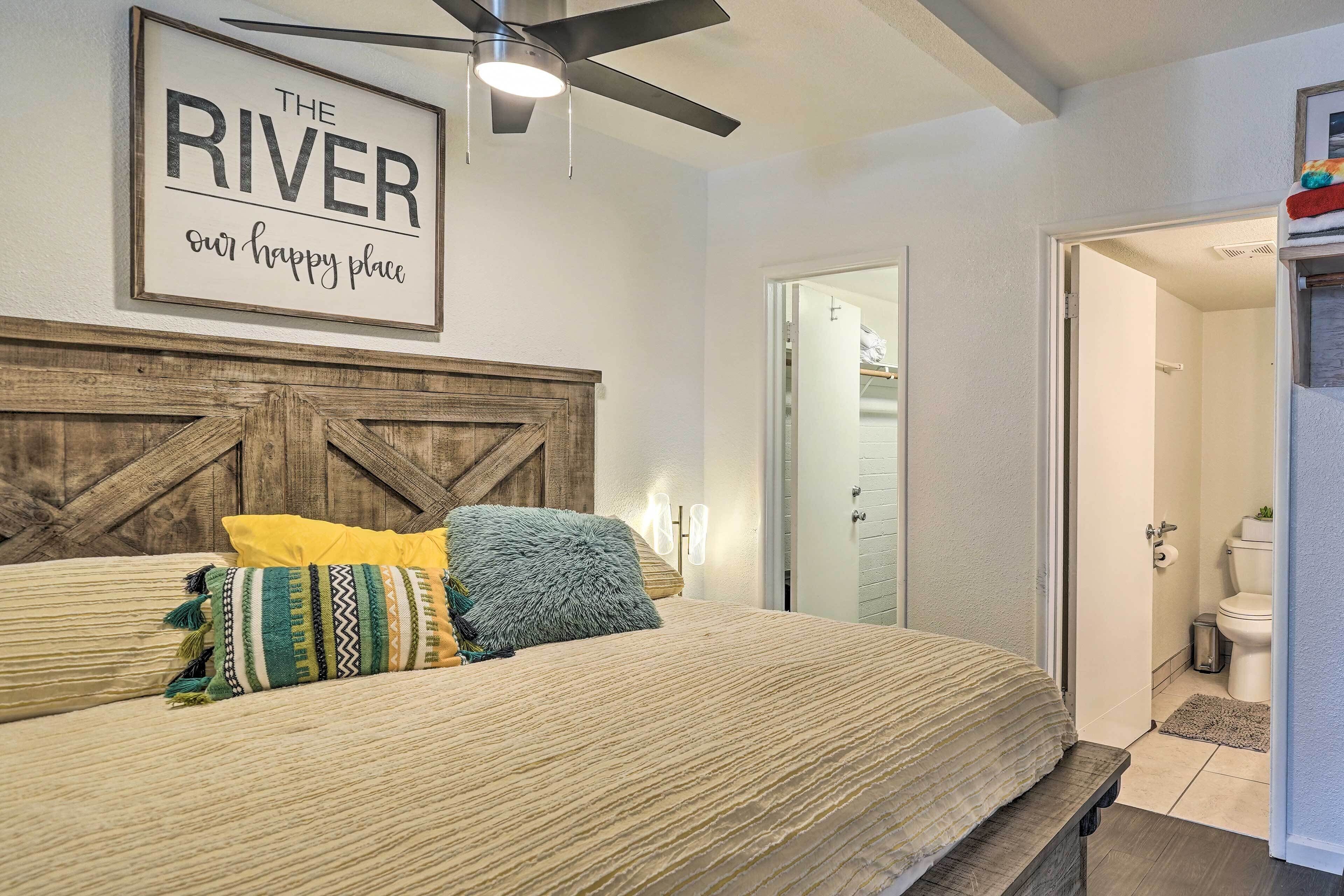 A bedroom with a bed, a wooden headboard, a ceiling fan, and a sign above the bed.