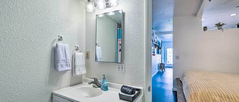 Un baño con lavamanos blanco, espejo y toallero.