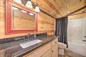 Une salle de bain avec un plafond en bois, un lavabo doté d’un plan de travail en granit, des toilettes blanches et une douche avec un rideau.