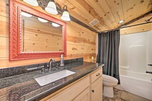Un baño con techo de madera, un lavamanos con encimera de granito, un inodoro blanco y una ducha con cortina.