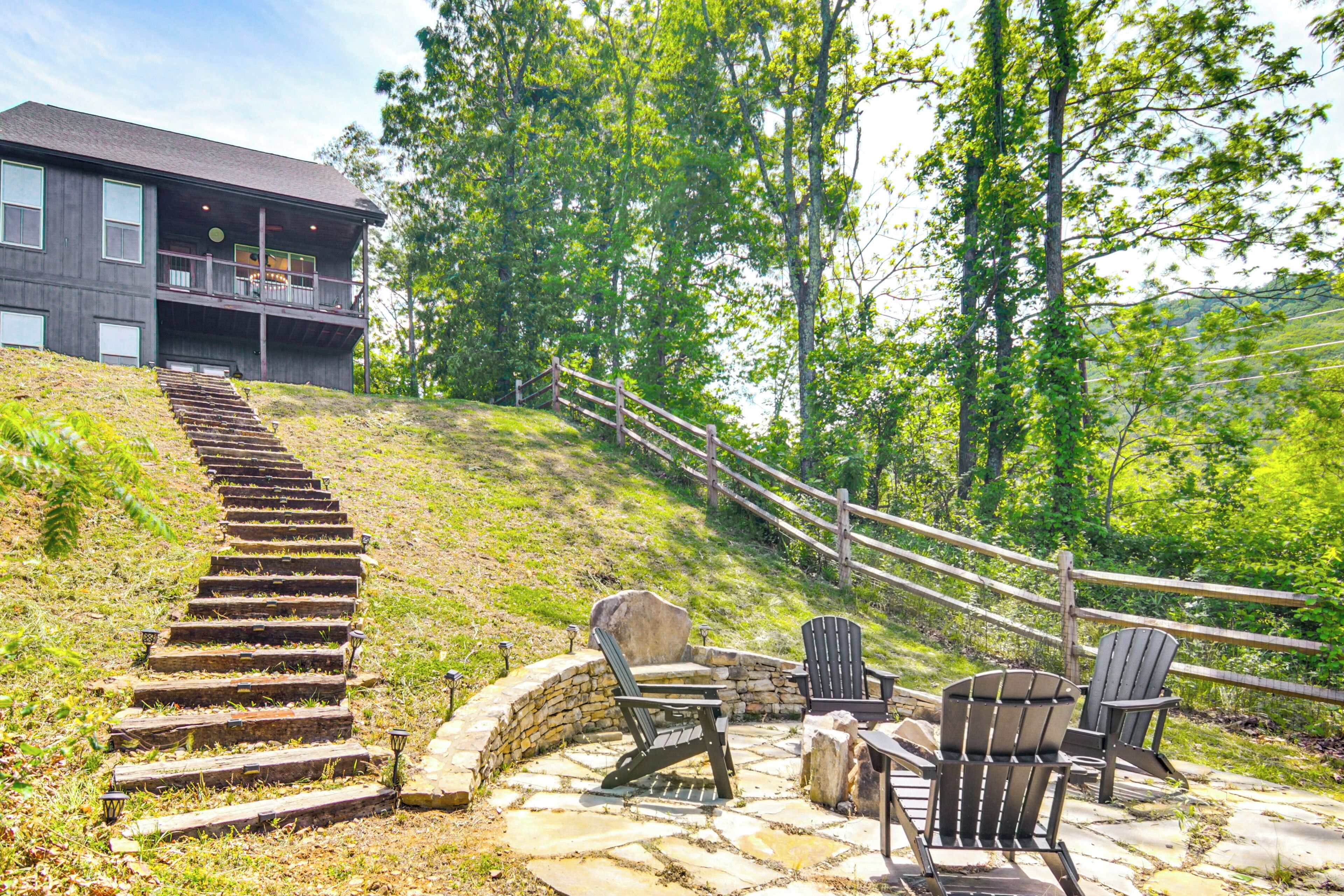 A stone staircase leading to a wooden deck with Adirondack chairs and a stone fire pit.
