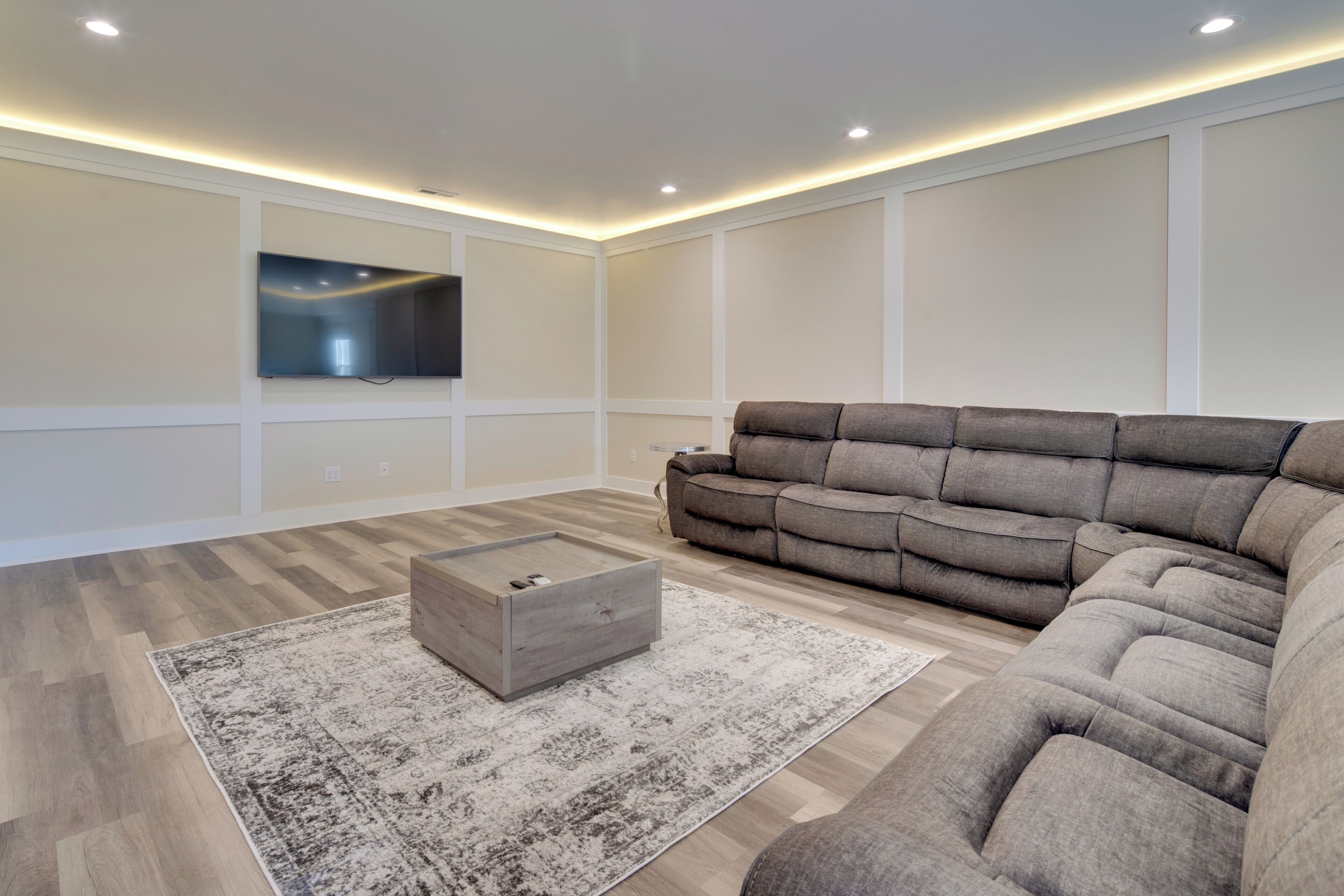 A modern living room with a sectional sofa, a wooden coffee table, and a large flat-screen TV mounted on the wall.
